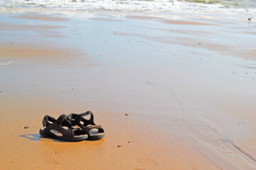 Obraz premium Pair of shoes or sandals left on a beach. Tide gradually coming in on flat sand.