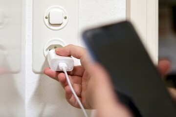 Plugging Phone Charger into electrical socket. Charging Phone Concept. 