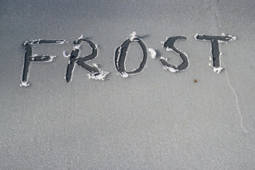The word frost scratched into the ice on a car windshield or windscreen in the winter.