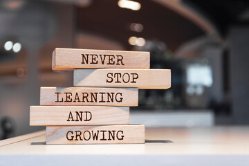 Wooden blocks with words 'Never stop learning and growing'. - obrazy, fototapety, plakaty