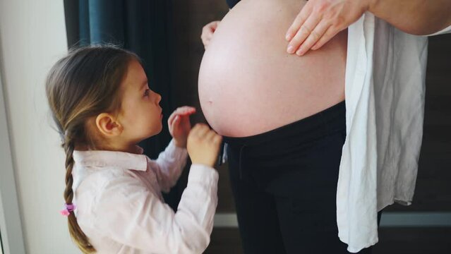 Little girl strokes her mother's belly with her future brother. Gently hugs pregnant mother, kisses
