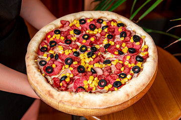 Tasty and big pizza with different types of meat. Pizza with sausage, ham, corn and olives.