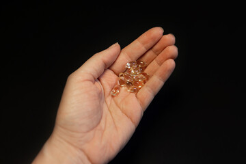 Vitamin E, D3, omega 3 gel capsules in a hand on a black background.