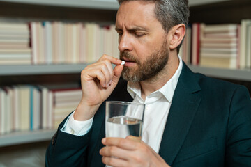 Close up portrait of man taking a medicine pill from headache migraine. Tired man suffering from headache after computer work, exhausted with closed eyes touching head, relieving pain, migraine.