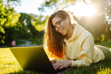 Smiling young woman with a laptop working or studying online on the background of a city building....
