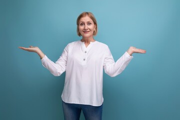 blonde 50s woman in a white blouse in menopause spreads her arms to the sides on a studio background