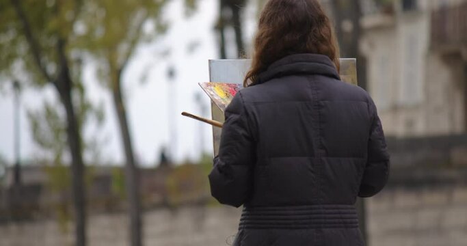 Woman painting a picture near the river Seine. Creative woman artist paints a picture with a brush while standing near the easel in Paris. Woman artist, art for sales, inspiration