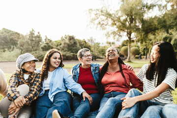 Happy multi generational group of women with different ethnicities having fun sitting on grass in a public park - Females empowerment concept - obrazy, fototapety, plakaty