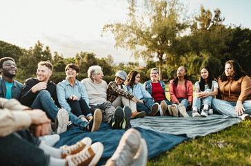 Happy multi generational people having fun sitting on grass in a public park - Diversity and friendship concept - obrazy, fototapety, plakaty