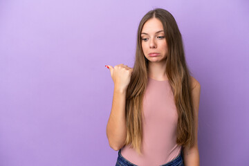 Young Lithuanian woman isolated on purple background unhappy and pointing to the side