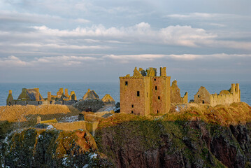 Fototapeta premium Snow seen on the cliffs on which Dunnottar Castle lies, lit up in the Golden Evening Sun of a cold Winters day in February.
