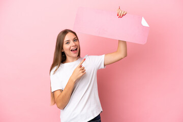 Young Lithuanian woman isolated on pink background holding an empty placard and pointing it