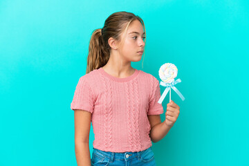 Little Caucasian girl holding a lollipop isolated on blue background looking to the side