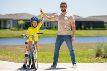 Obraz premium Happy Fathers day. Father and son in bike helmet for learning to ride bicycle at park. Father helping son cycling. Father and son on the bicycle on summer day. Kid son trying to ride bike with father.