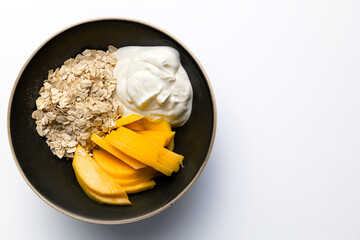 Healthy mango, oatmeal and yogurt breakfast bowl. Closeup isolated with white background and copy space.