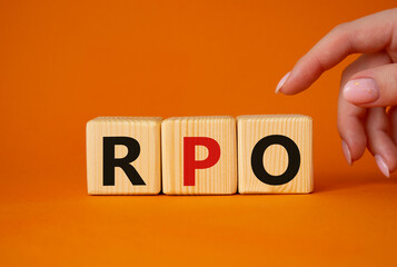 RPO - Recruitment Process Outsourcing symbol. Wooden cubes with words RPO. Businessman hand. Beautiful orange background. Business and RPO concept. Copy space.