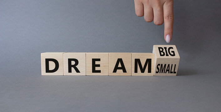 Dream Big vs Small symbol. Businessman Hand points at wooden cubes with words Dream Small and Dream Big. Beautiful grey background. Business and Dream concept. Copy space