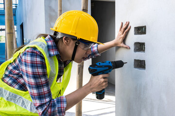 Engineer Construction woman using cordless screw driver working with wall in construction site 