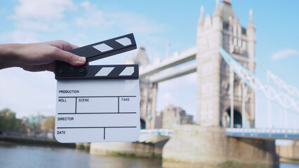 Hand is holding clapper board or movie slate with Tower Bridge background..