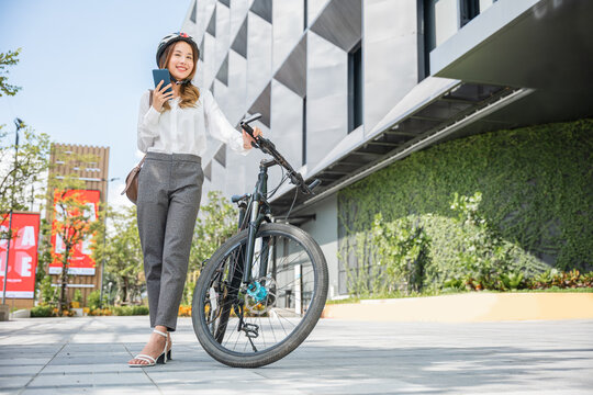 Asian smiling young woman with helmet hold mobile smart phone talk with business during go to office work at street with bicycle, Eco friendly, Lifestyle business female commuting outside in morning