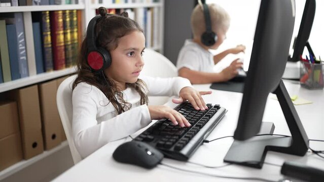 Adorable boy and girl students using computer and headphones studying at classroom