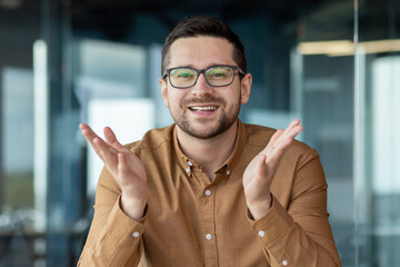 Close-up photo. Portrait of a smiling young male blogger sitting in the office in front of the camera and talking online on a video call, recording a podcast, conducting an online webinar
