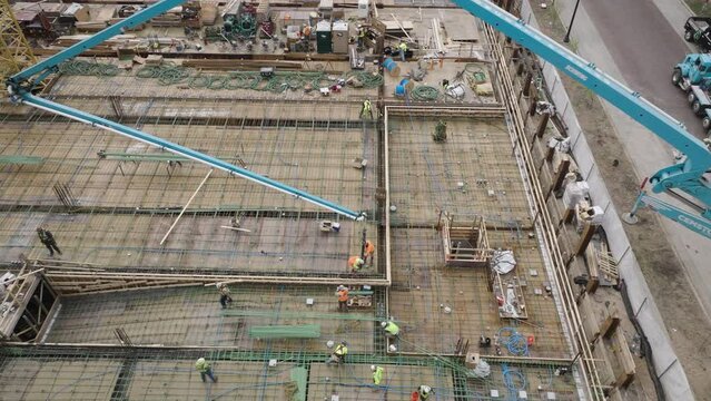 Aerial, concrete pump crane extending over building foundation construction site, workers pouring concrete
