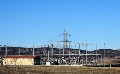 General view of an electrical substation in the middle of the countryside with many tall poles and wiring lines - Powered by Adobe