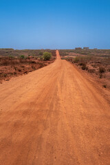 Fototapeta na wymiar Un route de terre rouge au Sénégal en Afrique de l'Ouest