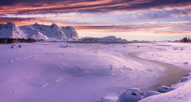 Wonderful snowy winter in Norway. Beautiful sunset with colorful dramatic sky, in amazing winter landscape of the Lofoten Islands. Snow-covered riverbed and mountains under sunlight. Creative image