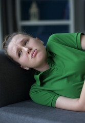 Worried young woman sit on sofa look aside lean forward with folded hands feel fear anxiety. Teen...