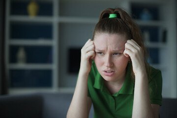 Worried young woman sit on sofa look aside lean forward with folded hands feel fear anxiety. Teen female stressed with unwanted pregnancy thinking on abortion hesitate have doubts making hard decision