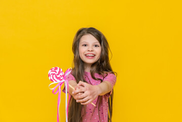 A happy little girl holds a caramel lollipop in her hands and smiles, a girl with a candy on an isolated yellow background.