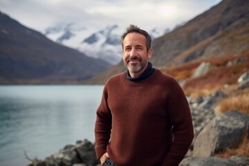 Environmental portrait photography of a pleased man in his 40s wearing a cozy sweater against a mountain lake or alpine background. Generative AI