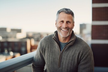 Portrait of smiling mature man standing on balcony at home in sunny day