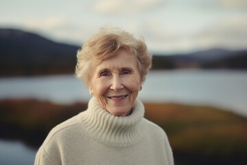 Fototapeta na wymiar Portrait of smiling senior woman on background of lake. Portrait of senior woman in sweater.