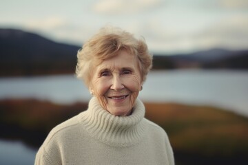 Fototapeta premium Portrait of smiling senior woman on background of lake. Portrait of senior woman in sweater.