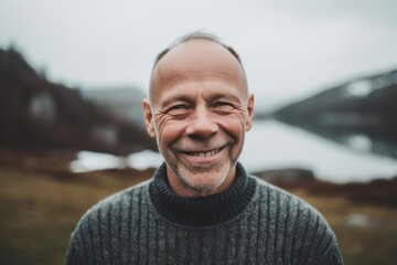 Portrait of a smiling senior man in the countryside. He is wearing a grey sweater.