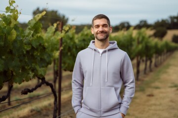 Environmental portrait photography of a pleased man in his 30s wearing a comfortable tracksuit against a vineyard or winery background. Generative AI