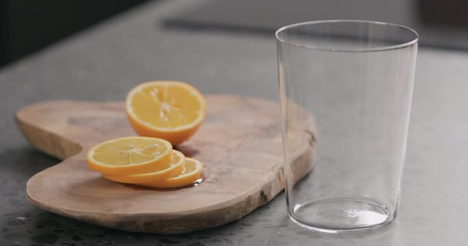 Slow motion pour water into glass with orange lemon on wood board