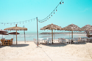 Wooden seaside parasols (Straw Umbrellas) and seats with table on the sand beach landscape in clear blue sky for vacation concept in summer holiday