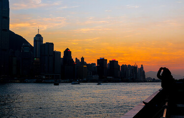 Silhouette of woman taking a picture of sunset over Hong Kong city skyline
