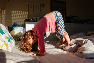 little girl stand with head down on parent's bed in the morning light