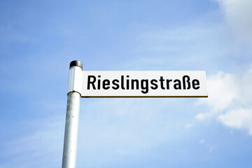 Straßenschild der Rieslingstraße mit Schrift in Schwarz auf weißem Grund mit blauem Himmel im...