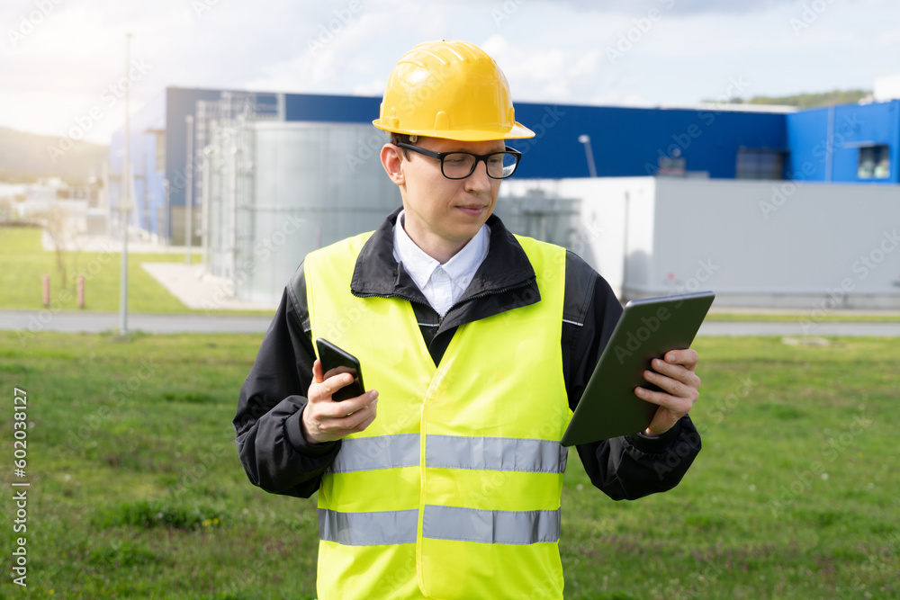 Poster Engineer with phone and digital tablet on a background of modern factory