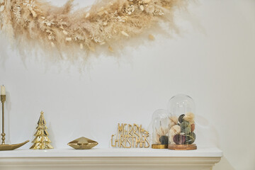 The mantelpiece with gold decor and a wreath above the fireplace made of dried flowers. Stylish minimalist interior with copy space. High quality photo