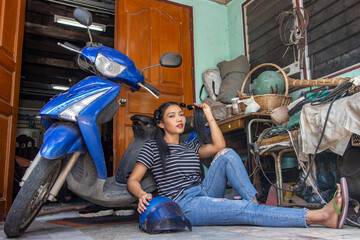 Plakat A young woman is sitting by a motorcycle parked in front of the entrance to a house