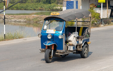 A traditional motor tricycle - tuk tuk rides on a rural road,Thailand