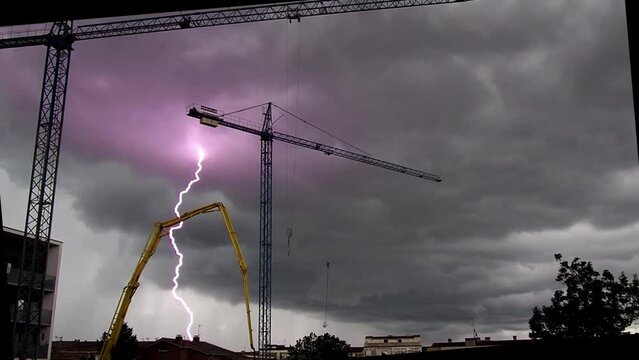Video of thunderstorm dark cloud lightning in a construction site with iron cranes.