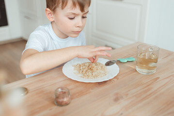 The boy eats at the dining table at home in the kitchen. He salts porridge from kiyon - the concept of children's healthy food.